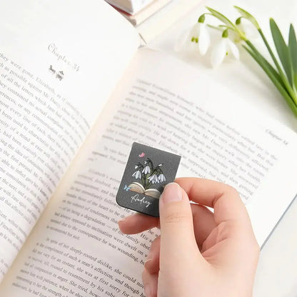 Person holding a black custom PU leather bookmark with floral design on an open book