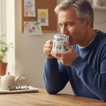 Man in a blue sweater holding a Personalized dad mug with a cartoon design, sitting at a table.