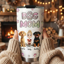 Person holding a custom tumbler with 'Dog Mom' design featuring cartoon characters and names in a cozy indoor setting.