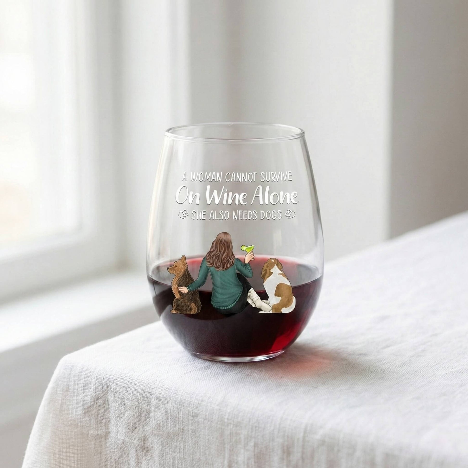 Personalized Stemless wine glass with a design of a woman and two dogs, filled with red wine, on a white surface.